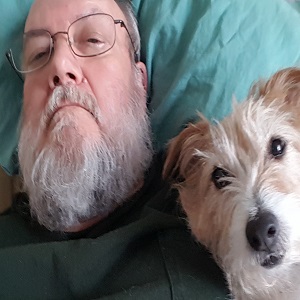 An older man lies on a blue pillow with a fluffy, small dog