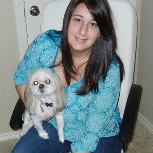 A woman named Elizabeth with dark hair and a blue shirt holding a small white dog